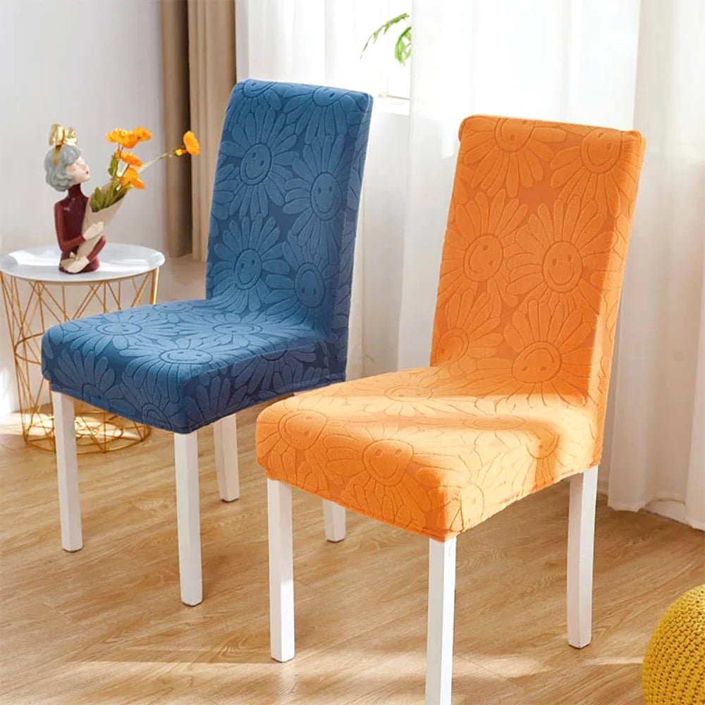 Two stretch chair covers in Sunburst Orange and Teal Breeze floral fabric with elastic fit, featuring a smiling daisy pattern, on dining chairs.