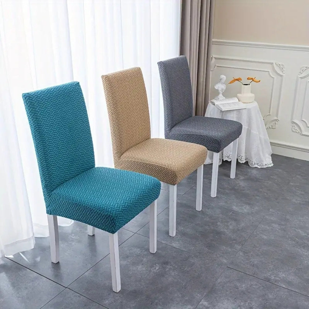 Three dining chairs showcasing Veluxe Haven Jacquard Velvet Dining Chair Covers with Stretch Fit in teal blue, cream beige, and charcoal gray. The covers feature a textured jacquard pattern and provide a snug fit.