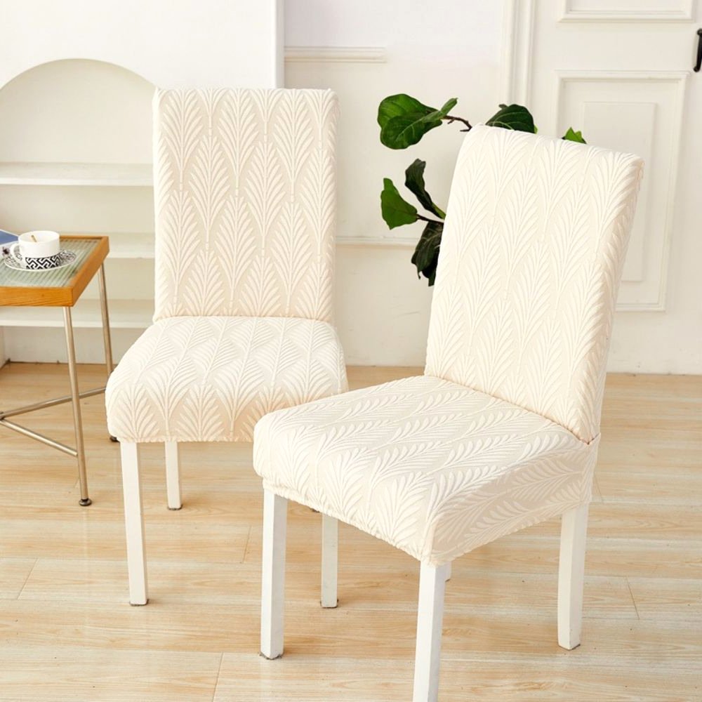 Two dining chairs covered in a soft white Velvet Haven elastic jacquard chair cover with a palm weave pattern, showcasing its stretch fit.