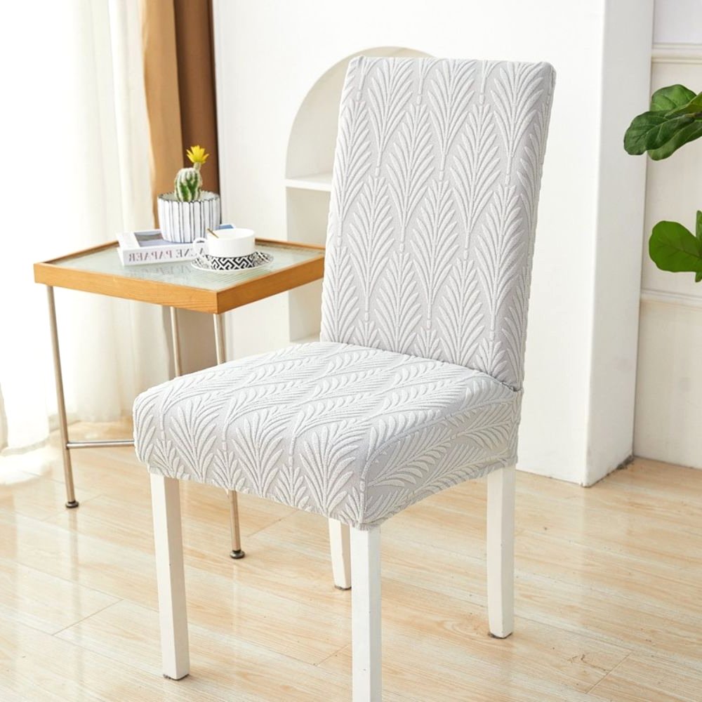 Velvet Haven Elastic Jacquard Chair Cover in Soft White Palm Weave pattern, shown on a white dining chair. This stretch fit furniture protector offers a modern design and easy installation.