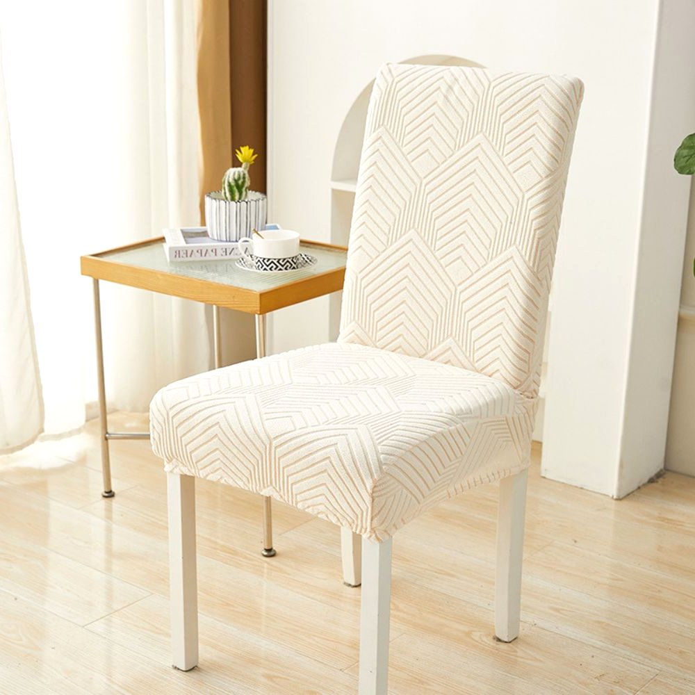 A warm beige Velvet Haven elastic jacquard chair cover with a Chevron Maze pattern on a white dining chair. The cover provides a stretch fit and modern design, suitable for furniture protection and home decor.