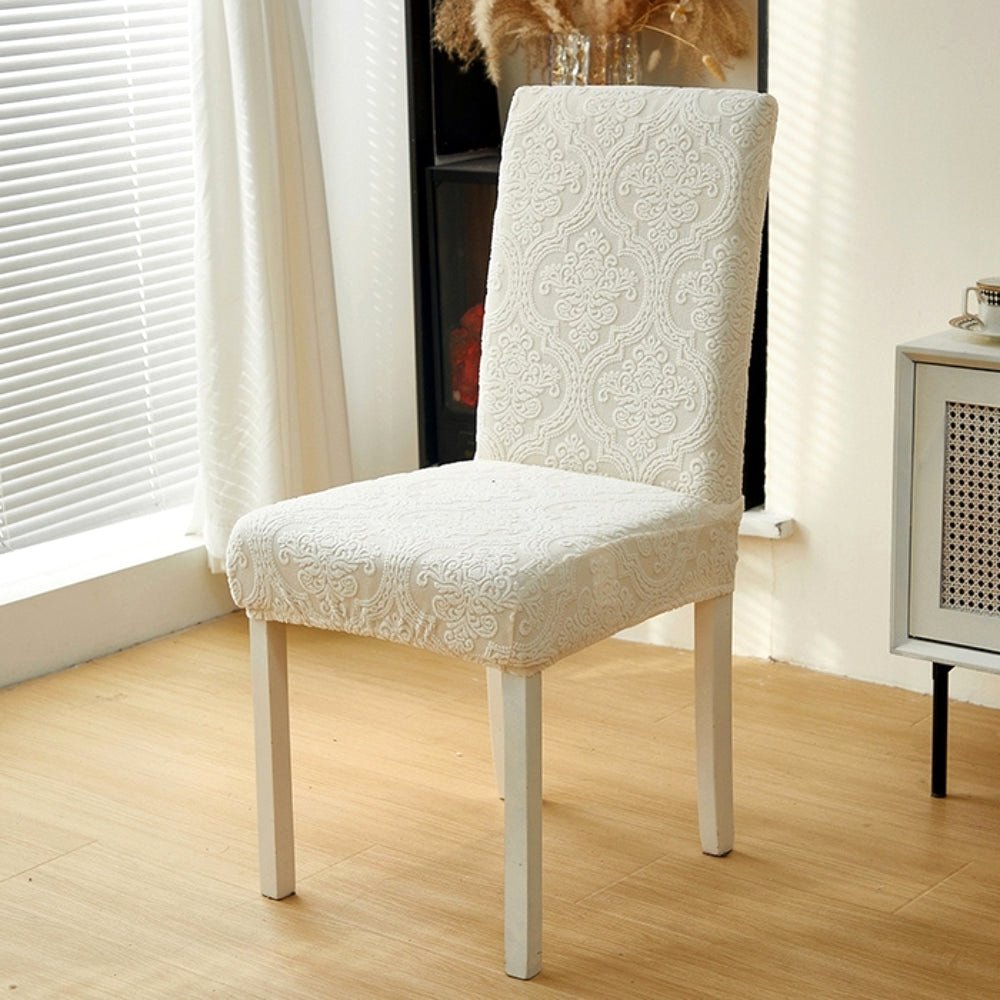 Elegant cream jacquard chair seat slipcover on a dining chair positioned near a window with blinds.