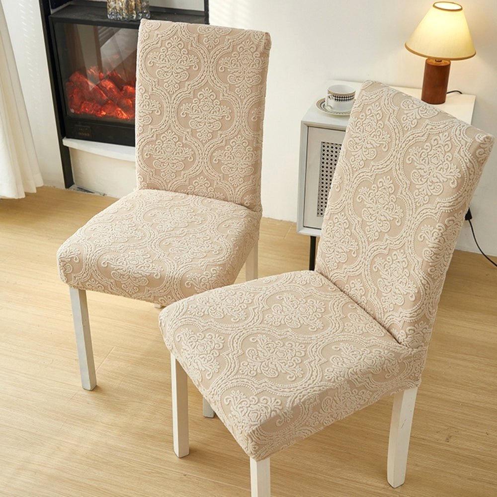 Two dining chairs covered in a Sand Bloom elegant jacquard stretch fit slipcover, displaying the warm beige tone and intricate pattern in a cozy living space.