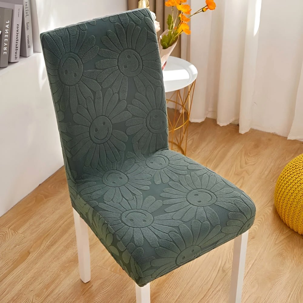 Mossy Shade Blossom Aura stretch chair cover featuring a floral daisy pattern with smiling faces on a white-legged chair in a home setting.