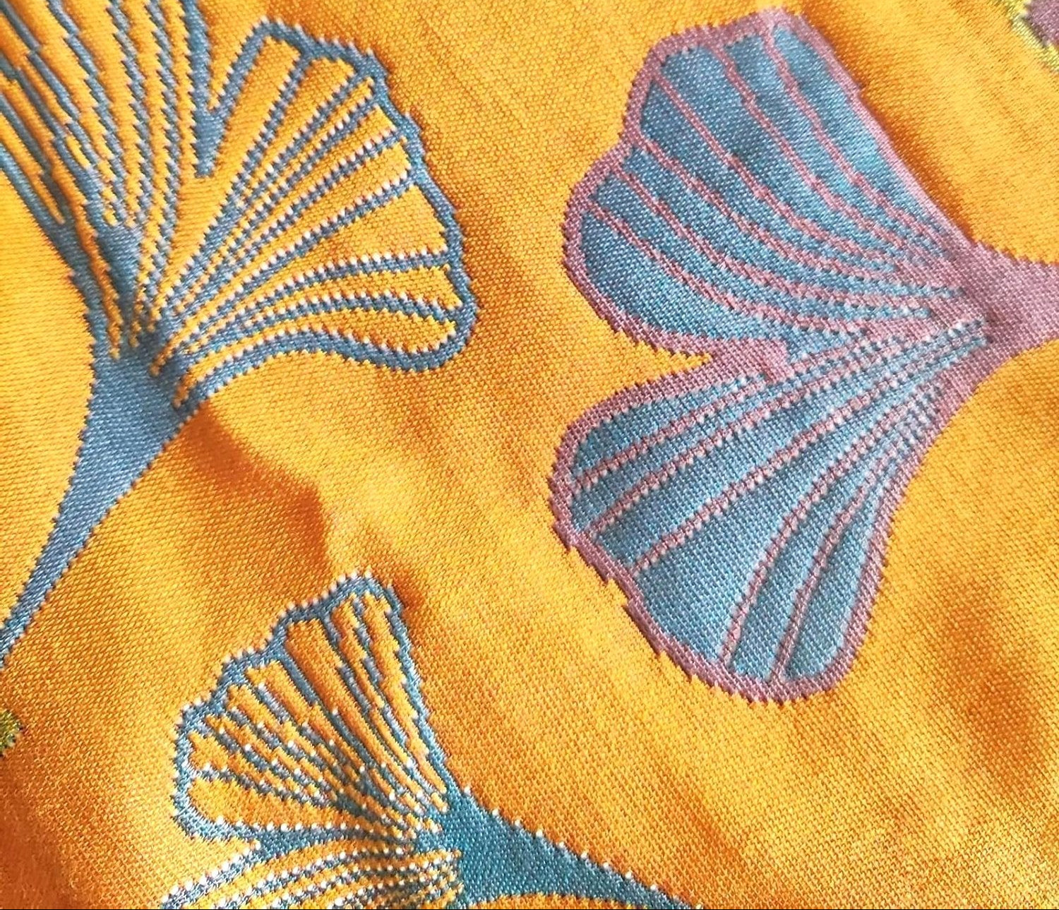 A close-up view of Ginkgo Haven cotton pillowcase fabric, showing intricate blue green embroidered ginkgo leaf patterns on a yellow background, highlighting its soft breathable texture.