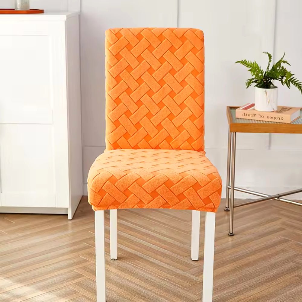 A single dining chair featuring a Sunset Orange Haven Weave Jacquard Chair Cover, showcasing its intricate woven pattern. The chair has white legs and is positioned in a bright room with a light wood floor and a white cabinet.