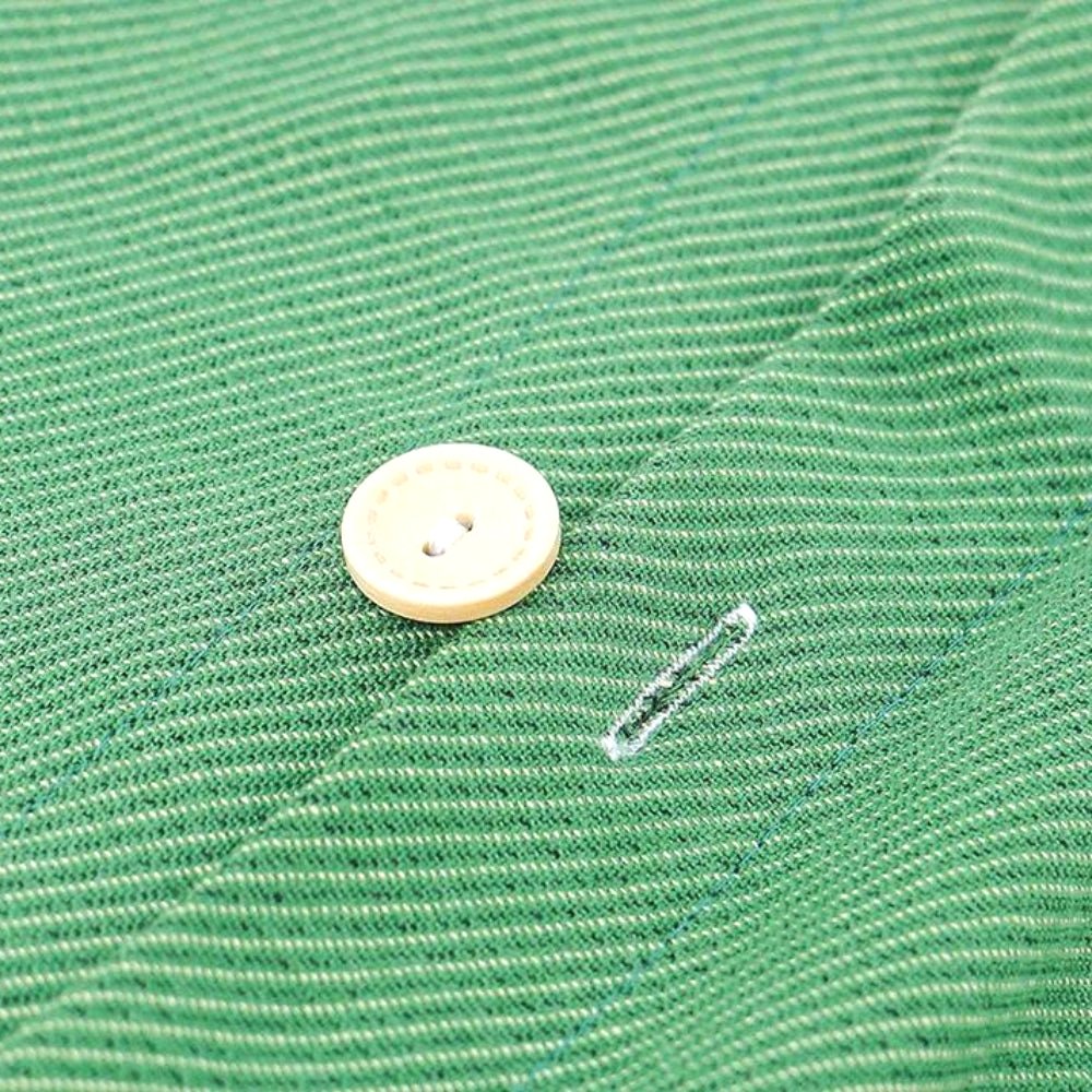 Close-up view of a wooden button and buttonhole on the green textured fabric of a Nordic Nest cotton gauze pillowcase, showcasing the quality and soft texture.