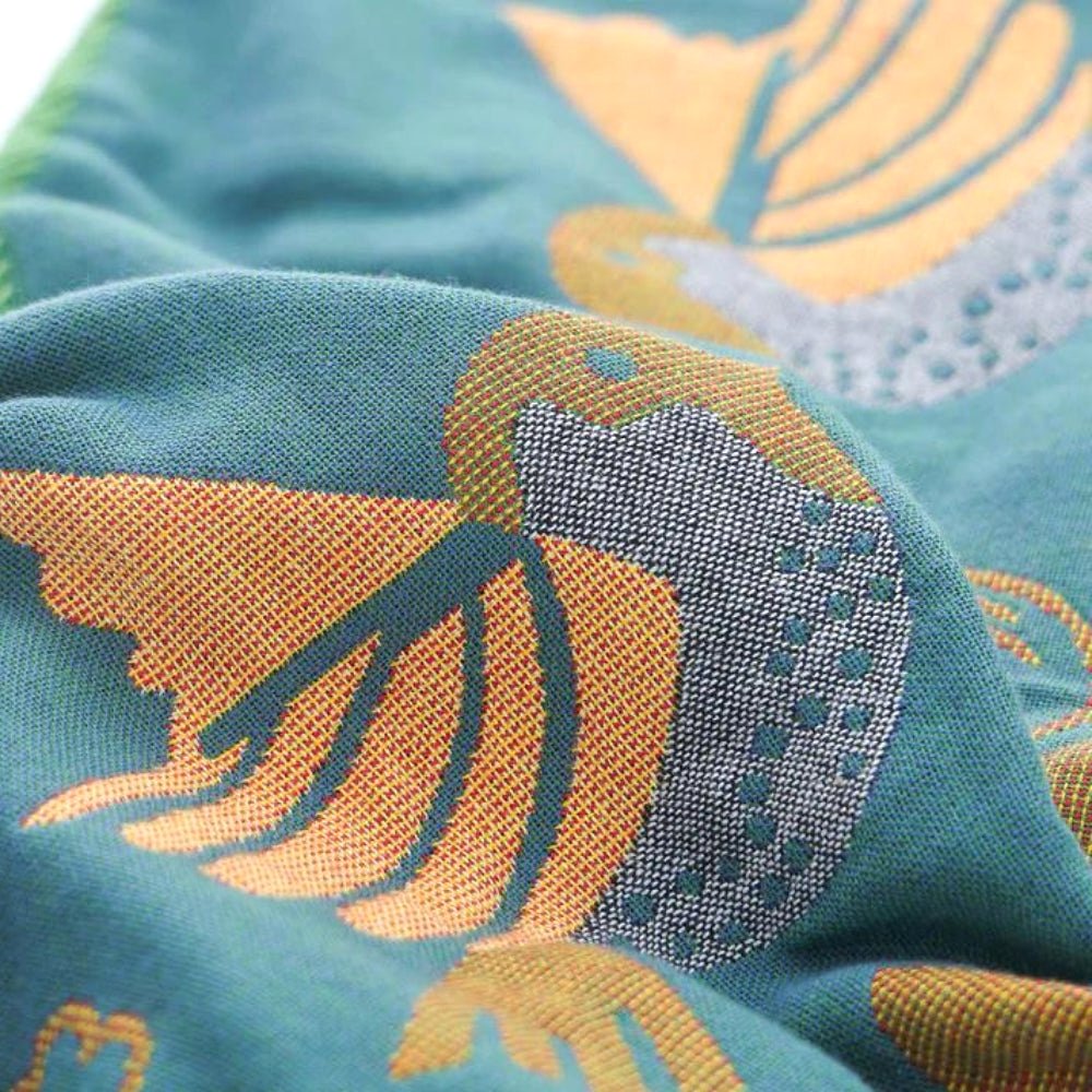 Extreme close-up of the teal Nordic Nest cotton gauze pillowcase, highlighting the intricate woven texture of the bird and leaf pattern, emphasizing its soft and breathable fabric.