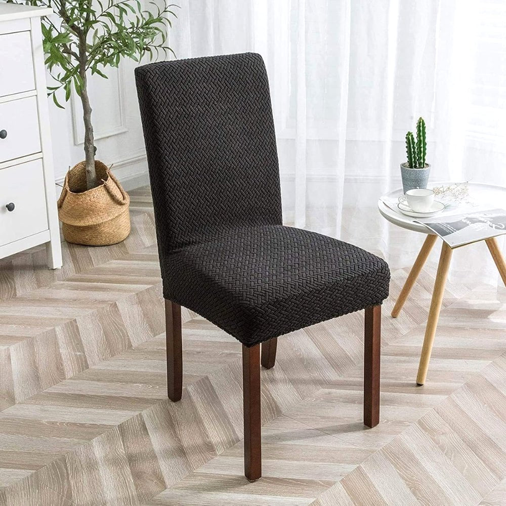 A deep black jacquard velvet stretch fit dining chair cover on a chair in a home setting, featuring a textured pattern and dark wooden legs.