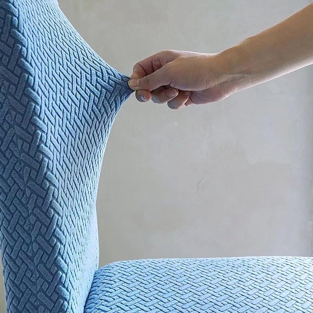 A hand stretching a Veluxe Haven Jacquard Velvet Dining Chair Cover in teal blue, demonstrating its flexible stretch fit and textured jacquard pattern.