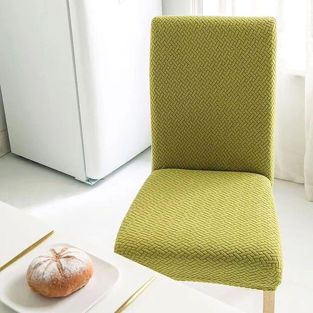 Olive Green Veluxe Haven Jacquard Velvet Dining Chair Cover with Stretch Fit, displayed on a dining chair in a kitchen or dining area with a pastry on a plate.