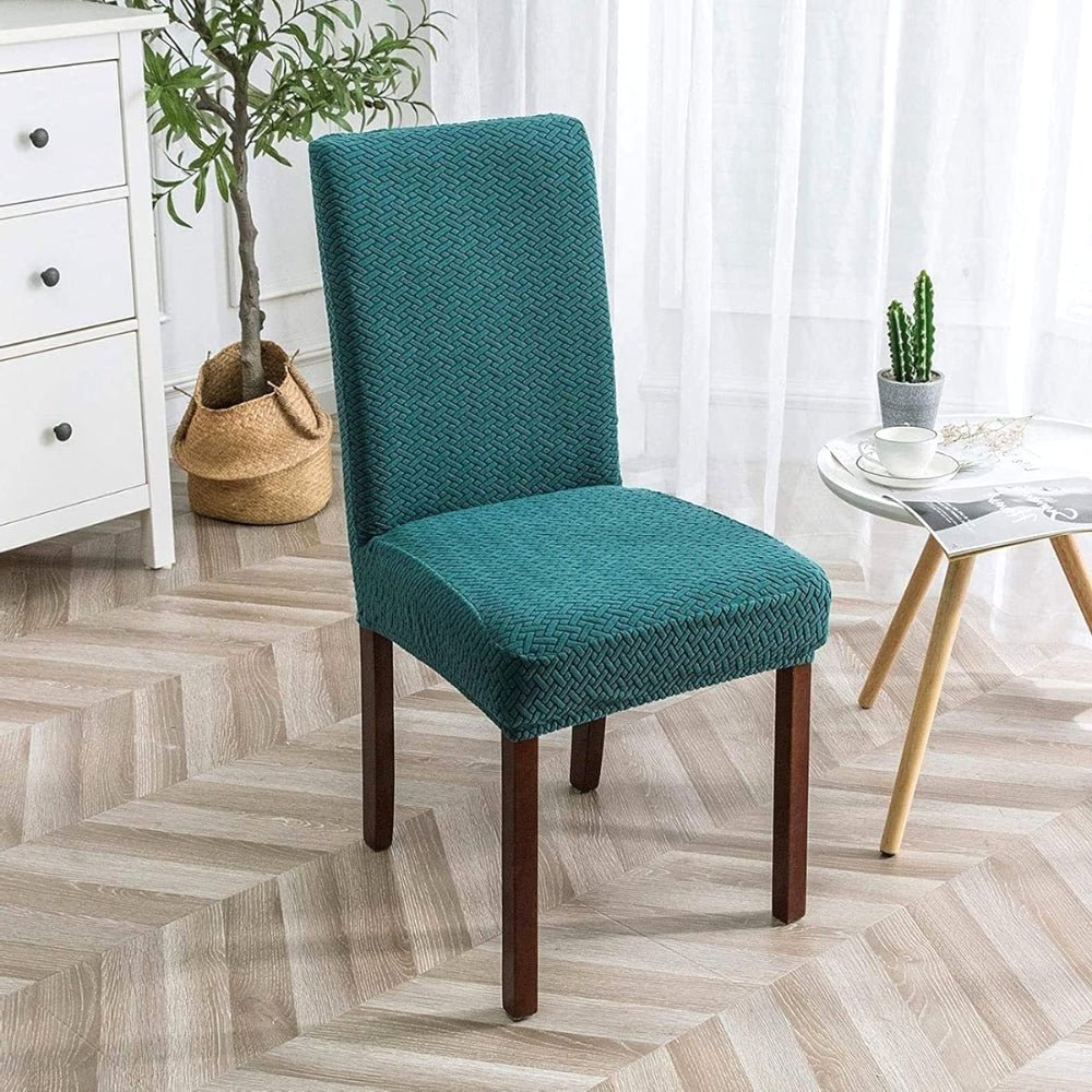 Teal Blue Veluxe Haven Jacquard Velvet Dining Chair Cover with Stretch Fit on a dining chair in a modern living room setting with a side table and plant.