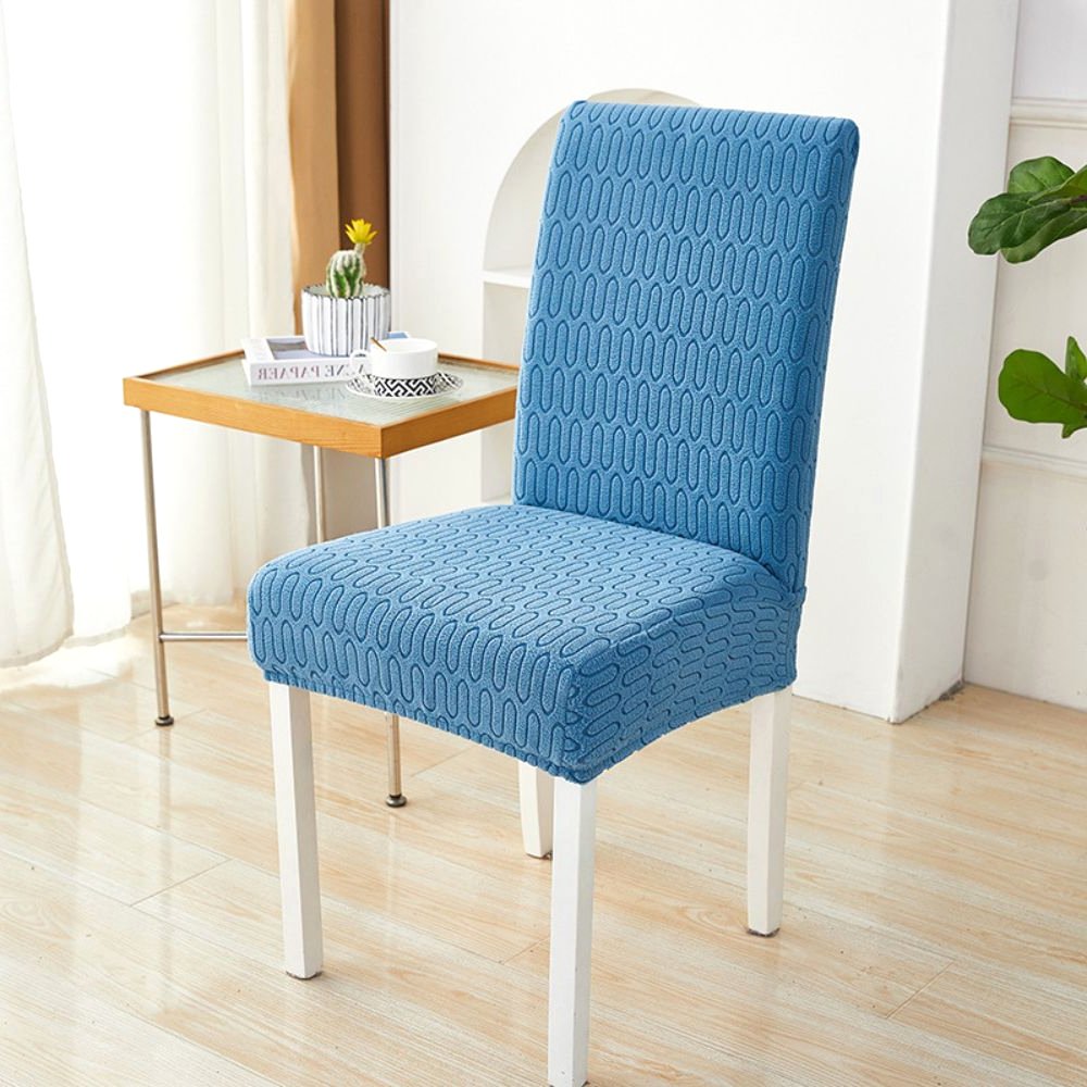 Ocean blue elastic jacquard chair cover with a chevron maze pattern, shown on a dining chair in a modern room setting with a side table and plant.