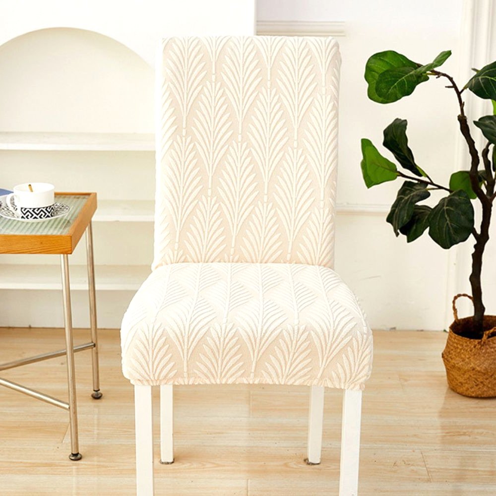 A single dining chair covered in a soft white Velvet Haven elastic jacquard chair cover with a palm weave pattern, demonstrating its snug fit.