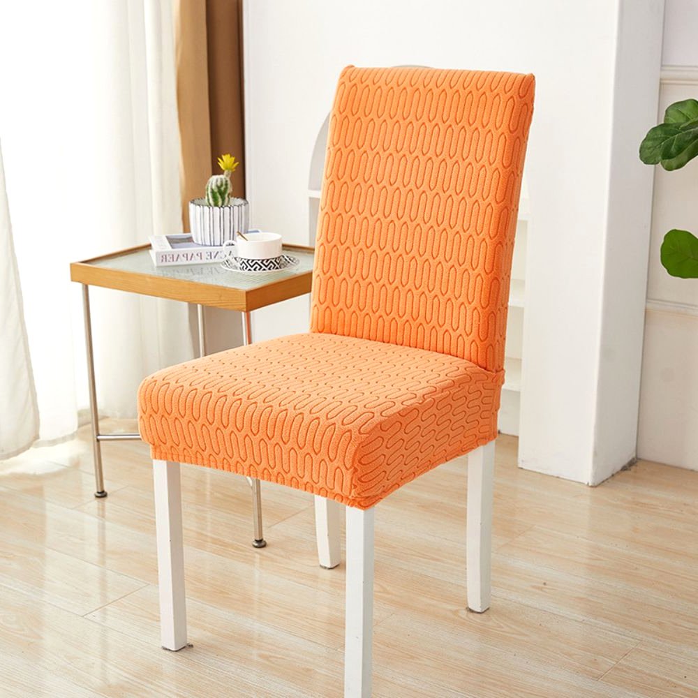 Sunset orange elastic jacquard chair cover with a chevron maze pattern, shown on a dining chair in a modern room setting with a side table and plant.