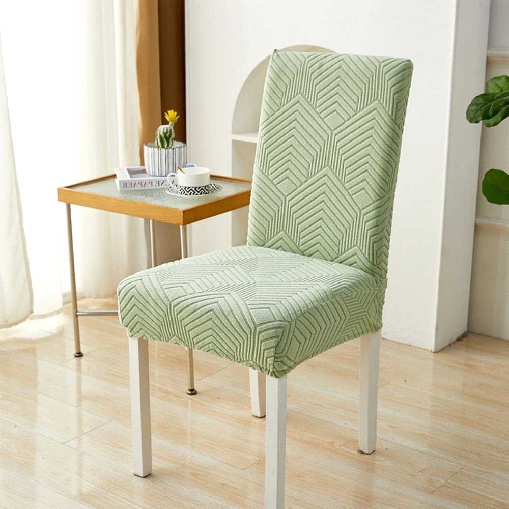 A sage green Velvet Haven elastic jacquard chair cover with a Chevron Maze pattern on a white dining chair. The cover provides a stretch fit and modern design, suitable for furniture protection and home decor.