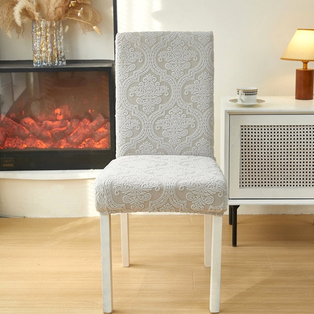 Elegant ash mist jacquard chair seat slipcover on a dining chair in a living room setting with a fireplace and side table.