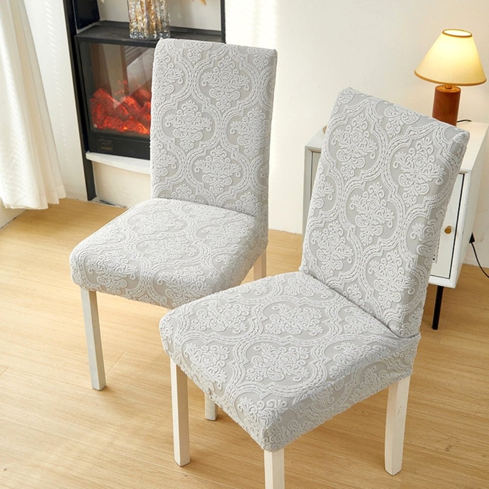 Two dining chairs covered in an Ash Mist elegant jacquard stretch fit slipcover, showcasing the intricate pattern and texture in a modern living room setting.