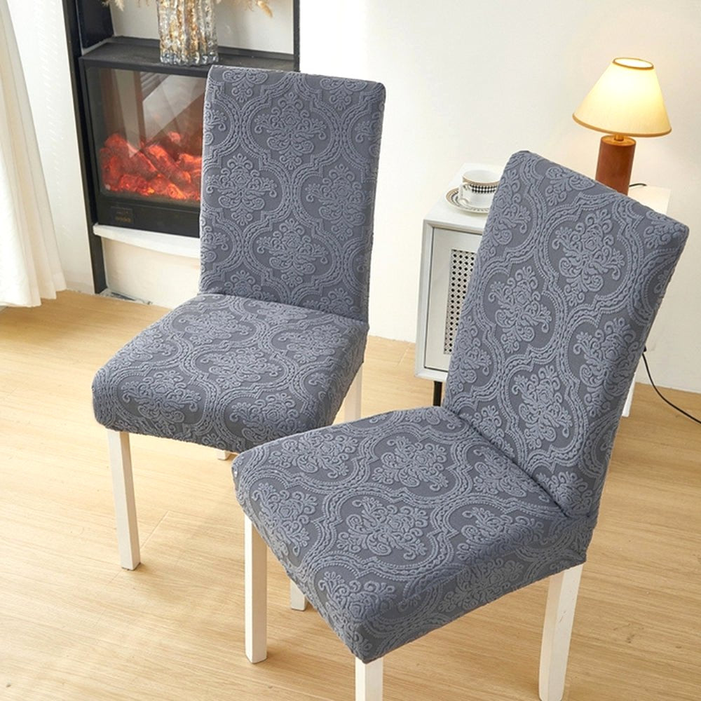 Two dining chairs covered in a Midnight Slate elegant jacquard stretch fit slipcover, highlighting the dark grey color and detailed pattern in a contemporary home.