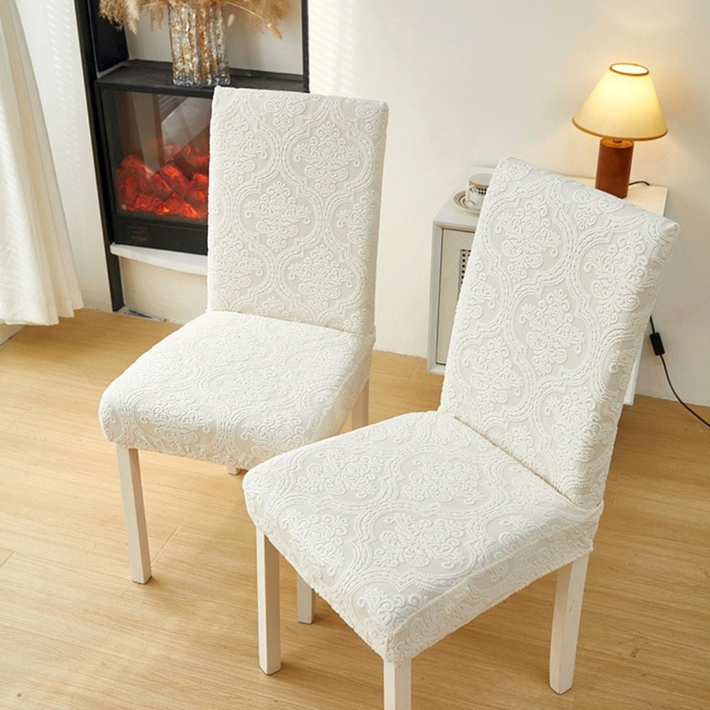Two elegant cream jacquard chair seat slipcovers on dining chairs in a living room setting with a fireplace and side table.
